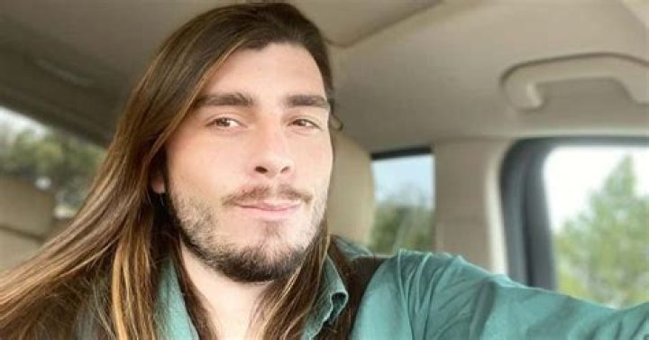 Andrew Kenton In 90 Day Fianc&eacute; wearing black shirt in front of plant