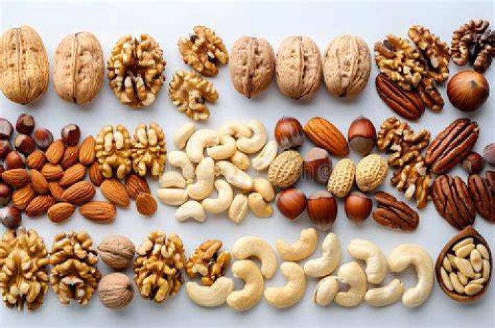 assorted nuts of almond,cashew,hazelnut,pistachio and walnut mixed in a wood bowl on brown wood table directly above view