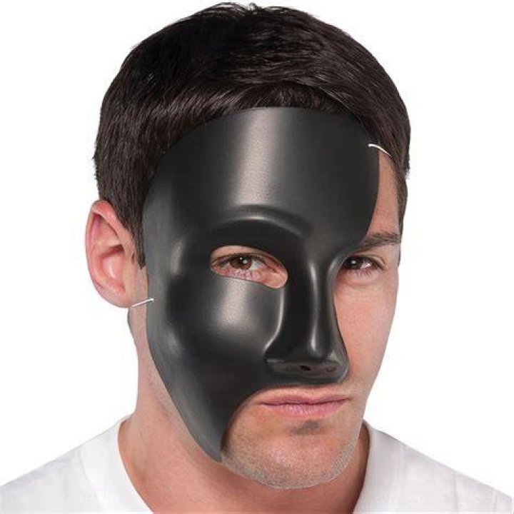 Black Mask standing in front of a fire.