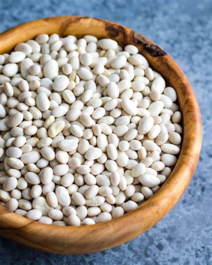 dried white beans in a blue ceramic plate on the background of a wooden kitchen table vegetarian and vegan food and diet cooking, home life harvesting growing organic farm products vegetable protein