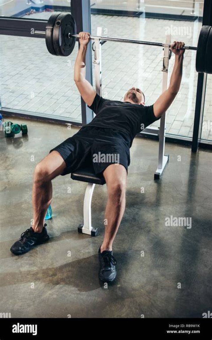 man in the gym lying on the floor barefoot wearing sportswear stretching for training, side view