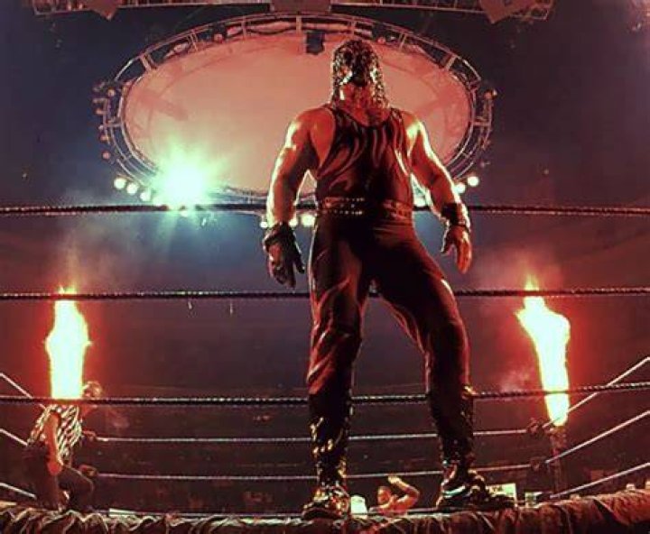 Masked Kane standing in the ring while the Titantron shows an image of him