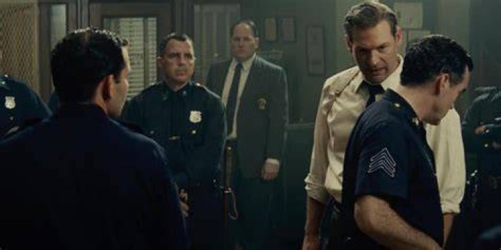 Officer Krupke smelling a drink while surrounded by Sharks in West Side Story 2021