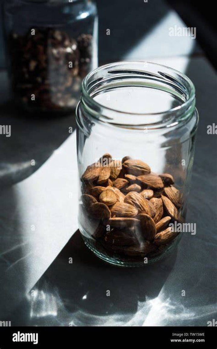raw almonds in a jar, a glass of almond milk, and a few of raw almonds scattering on the table