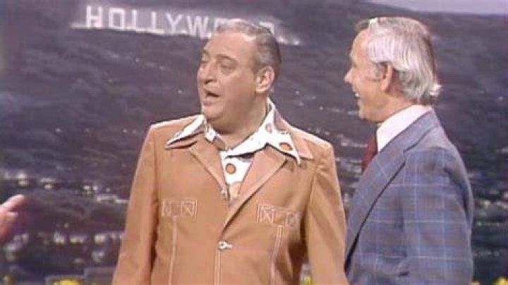 Rodney Dangerfield wearing a green shirt with people in the background