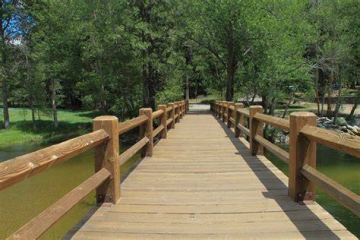 wooden bridge over blue water leading to small, tree covered island